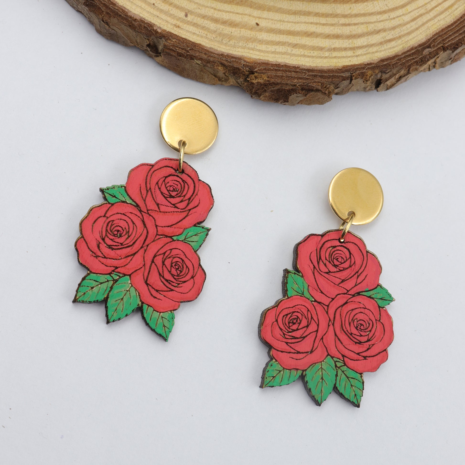 Red rose earrings with gold posts on a wooden surface
