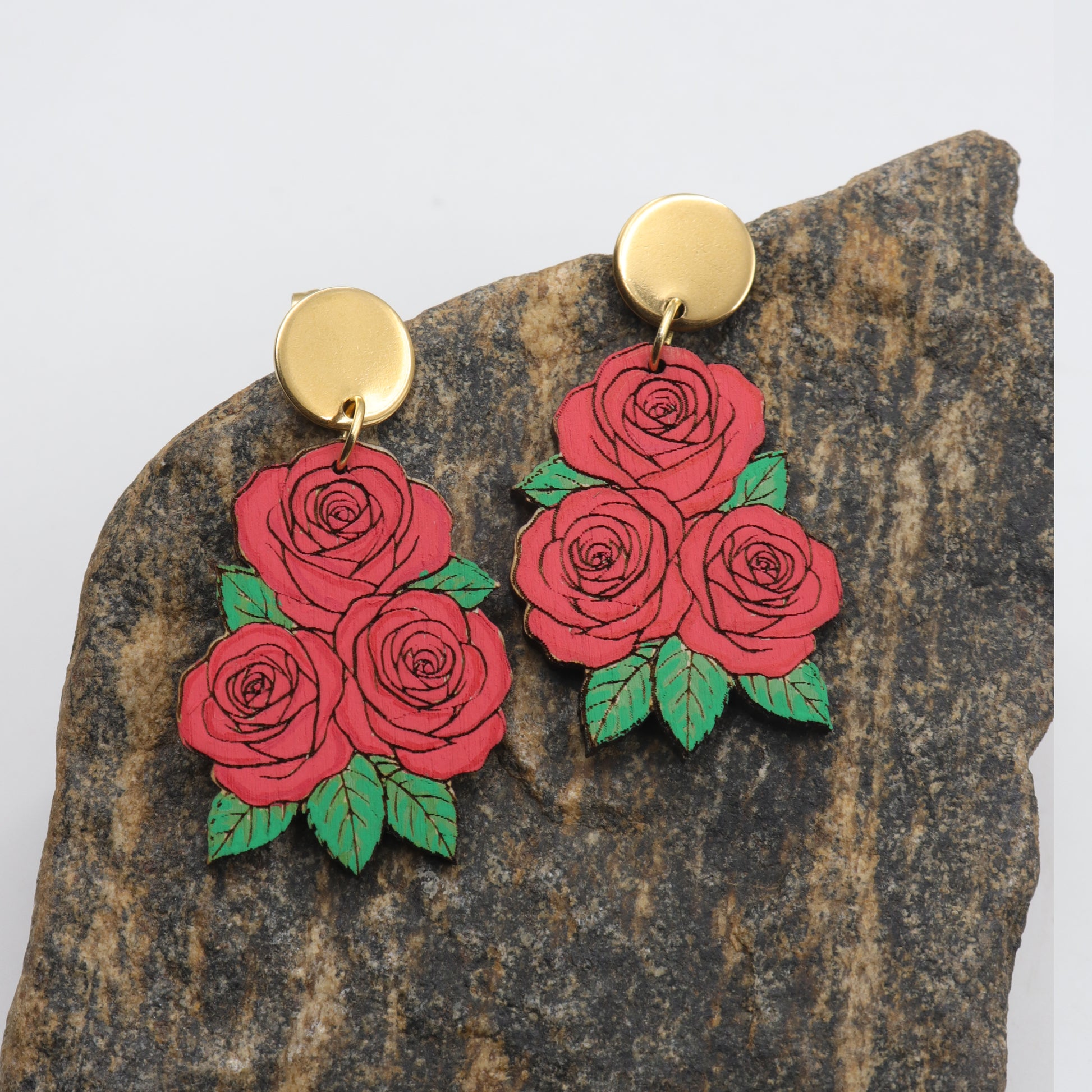 Red rose earrings with gold posts on a stone background