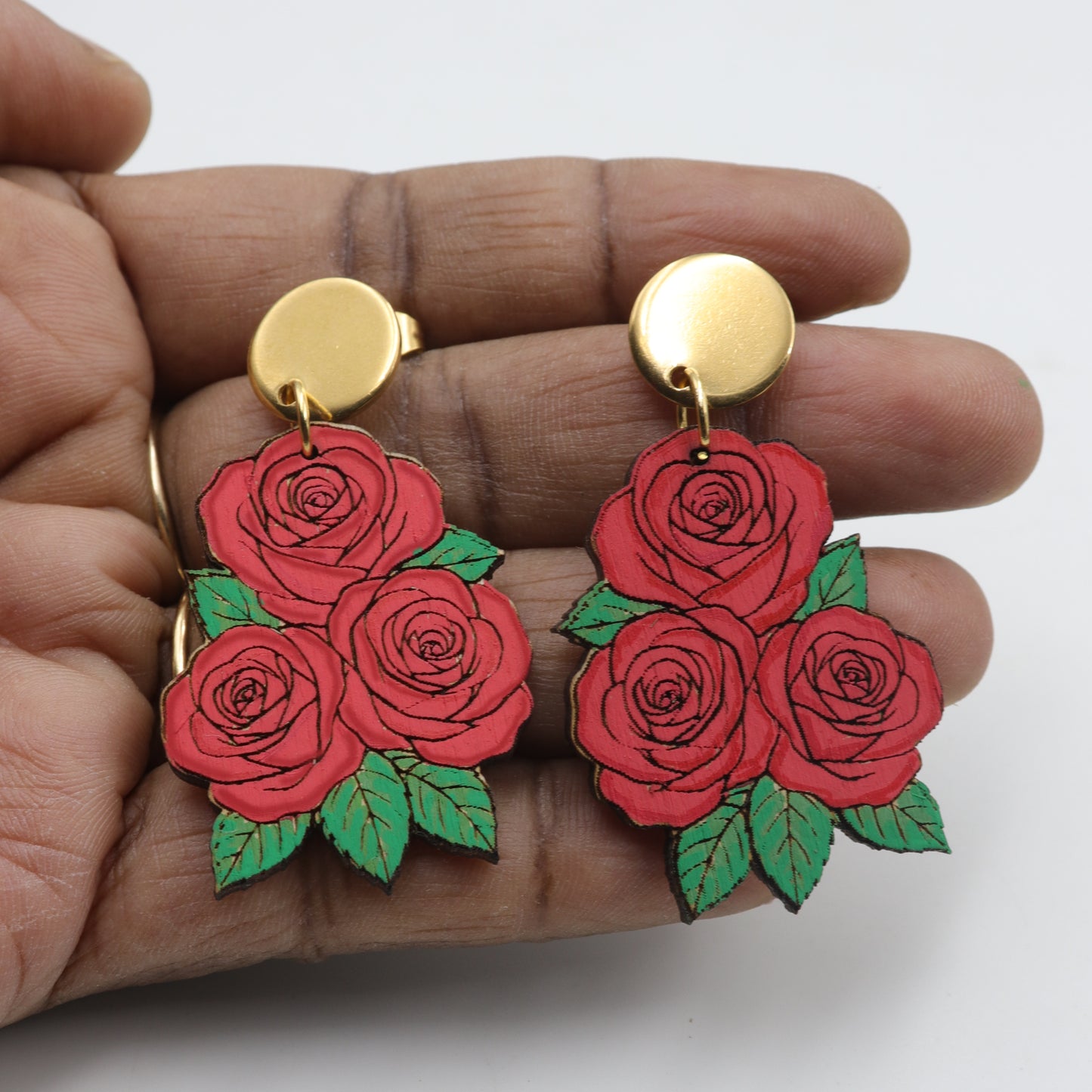 Red rose earrings with gold posts held between fingers on a white background