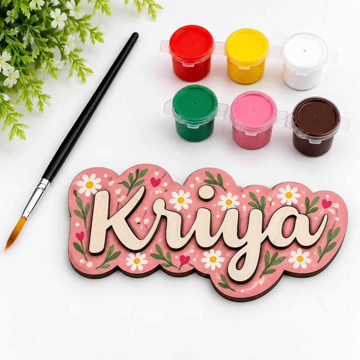 DIY paint-your-own wooden name fridge magnet with hand-painted floral design, acrylic paint pots, and paintbrush