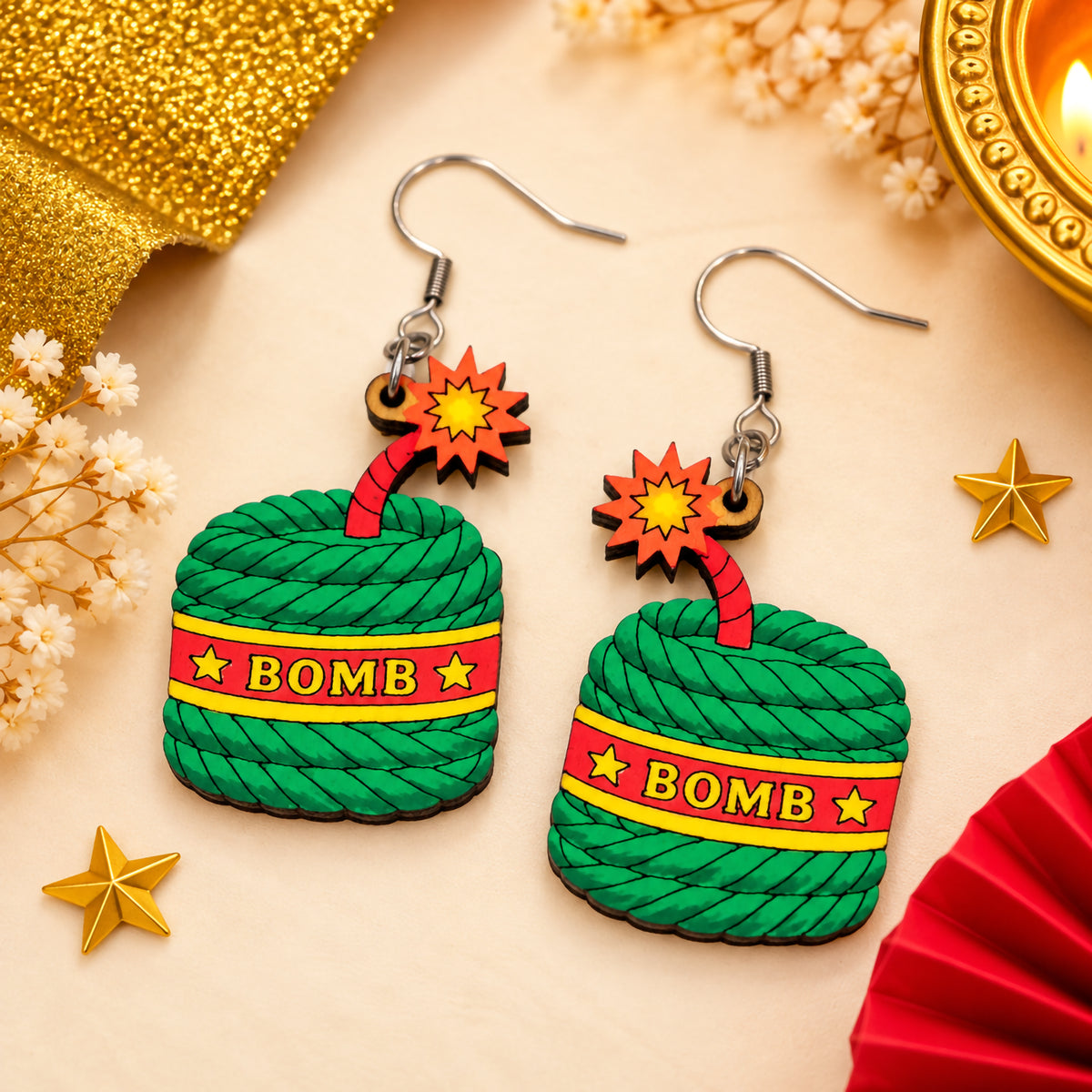 Hand-painted wooden Diwali bomb cracker earrings with green textured bodies, red BOMB bands, yellow stars and red starburst charms.