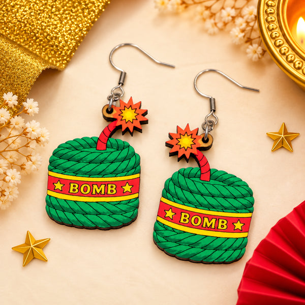 Hand-painted wooden Diwali bomb cracker earrings with green textured bodies, red BOMB bands, yellow stars and red starburst charms.