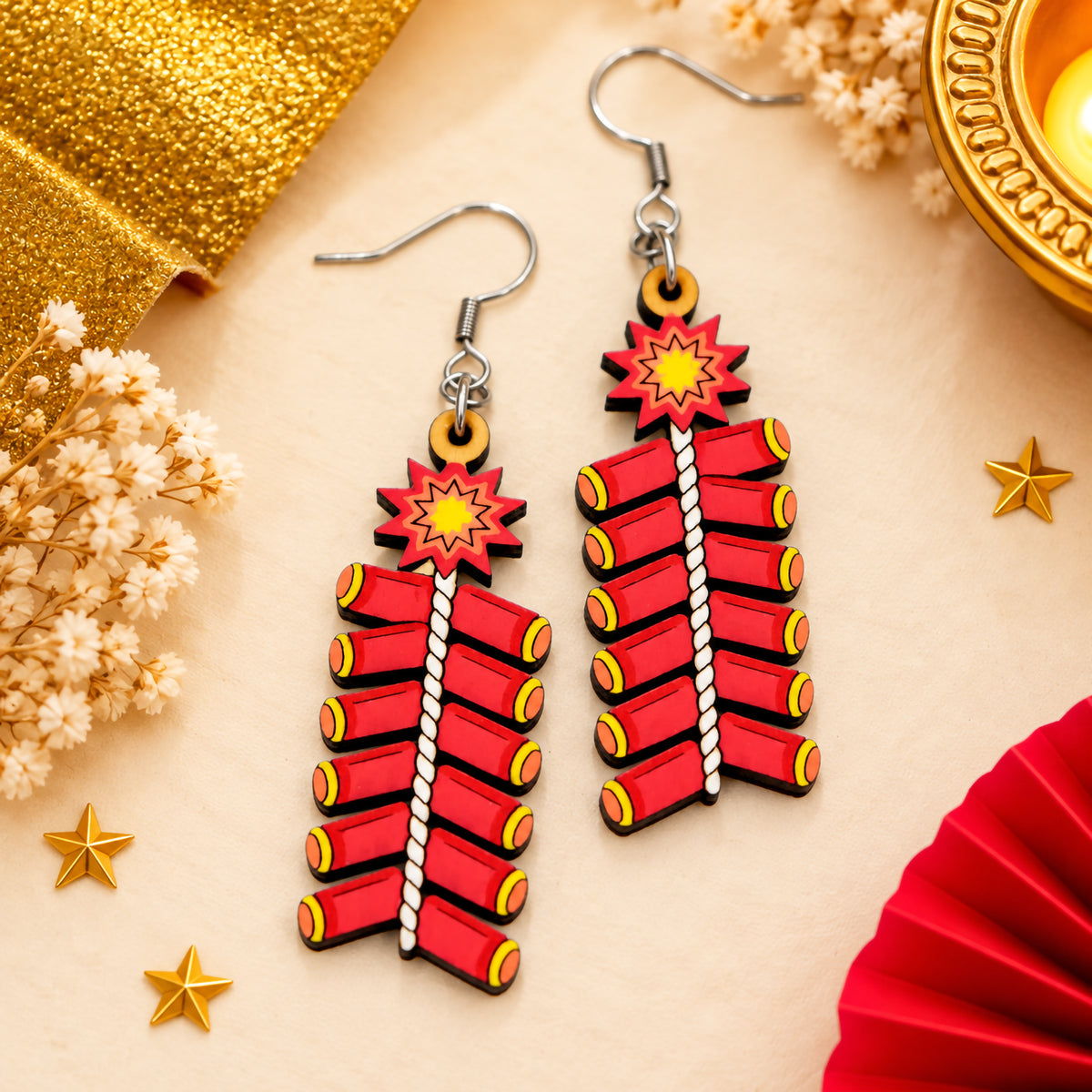 Hand-painted wooden Diwali ladi earrings featuring rows of red firecrackers, yellow ends, white twisted fuses and starburst charms.