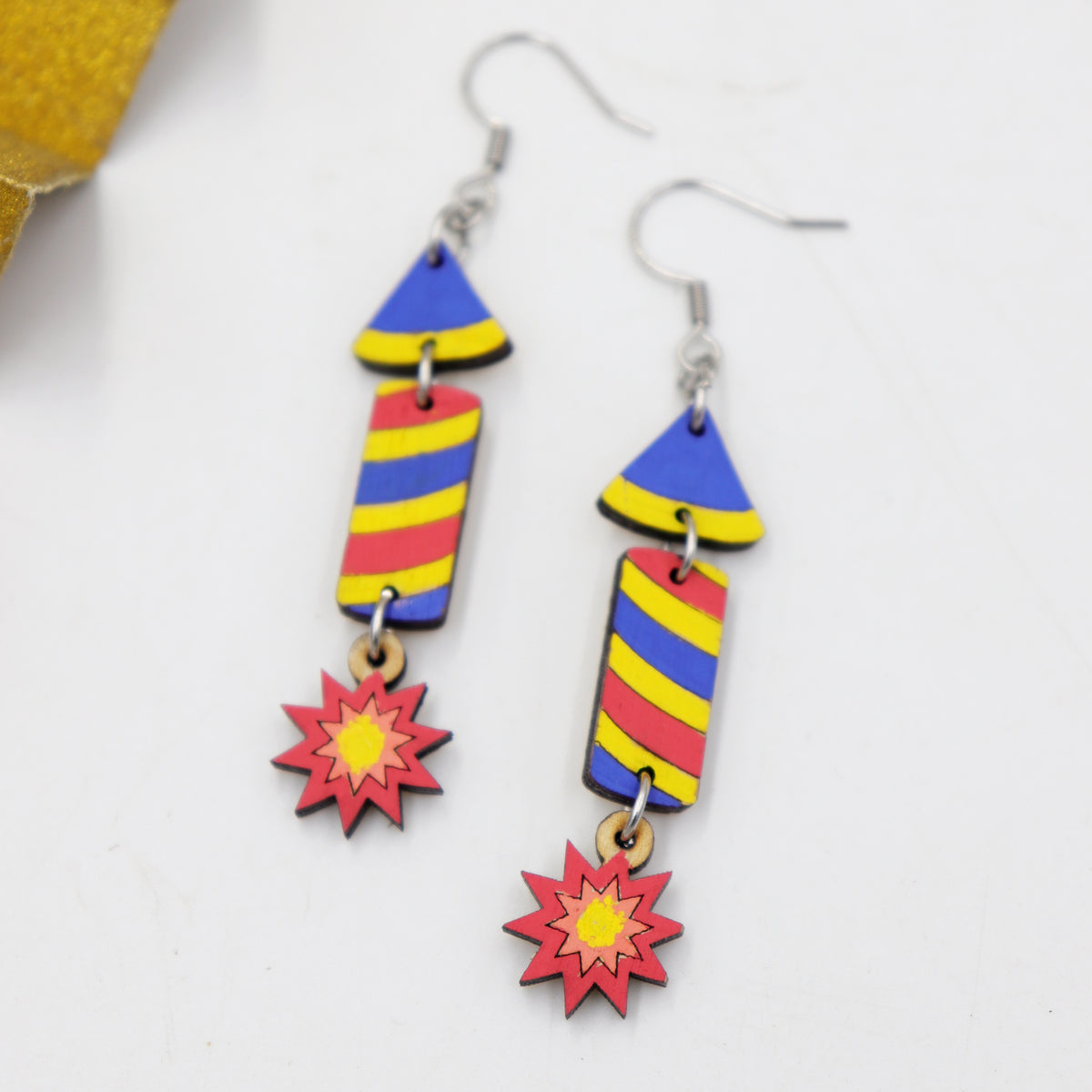 Hand-painted wooden Diwali rocket firework dangle earrings with colorful stripes and starburst, handmade by Mekala Crafts