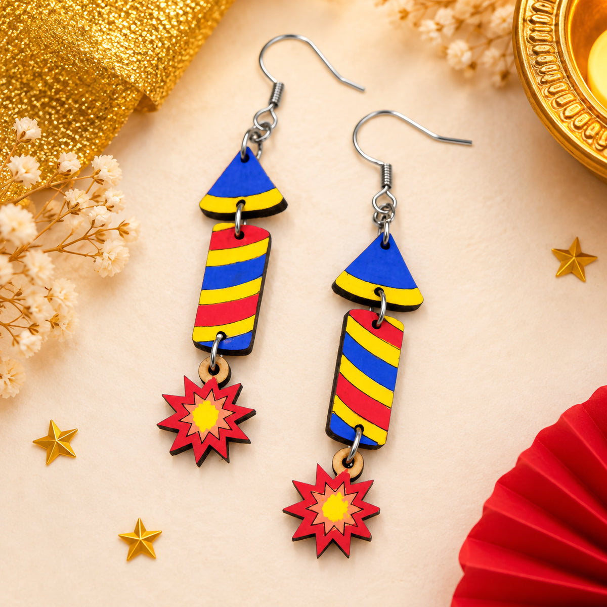 Hand-painted wooden Diwali rocket earrings with blue, yellow and red stripes and red starburst charms, finished with silver hooks.