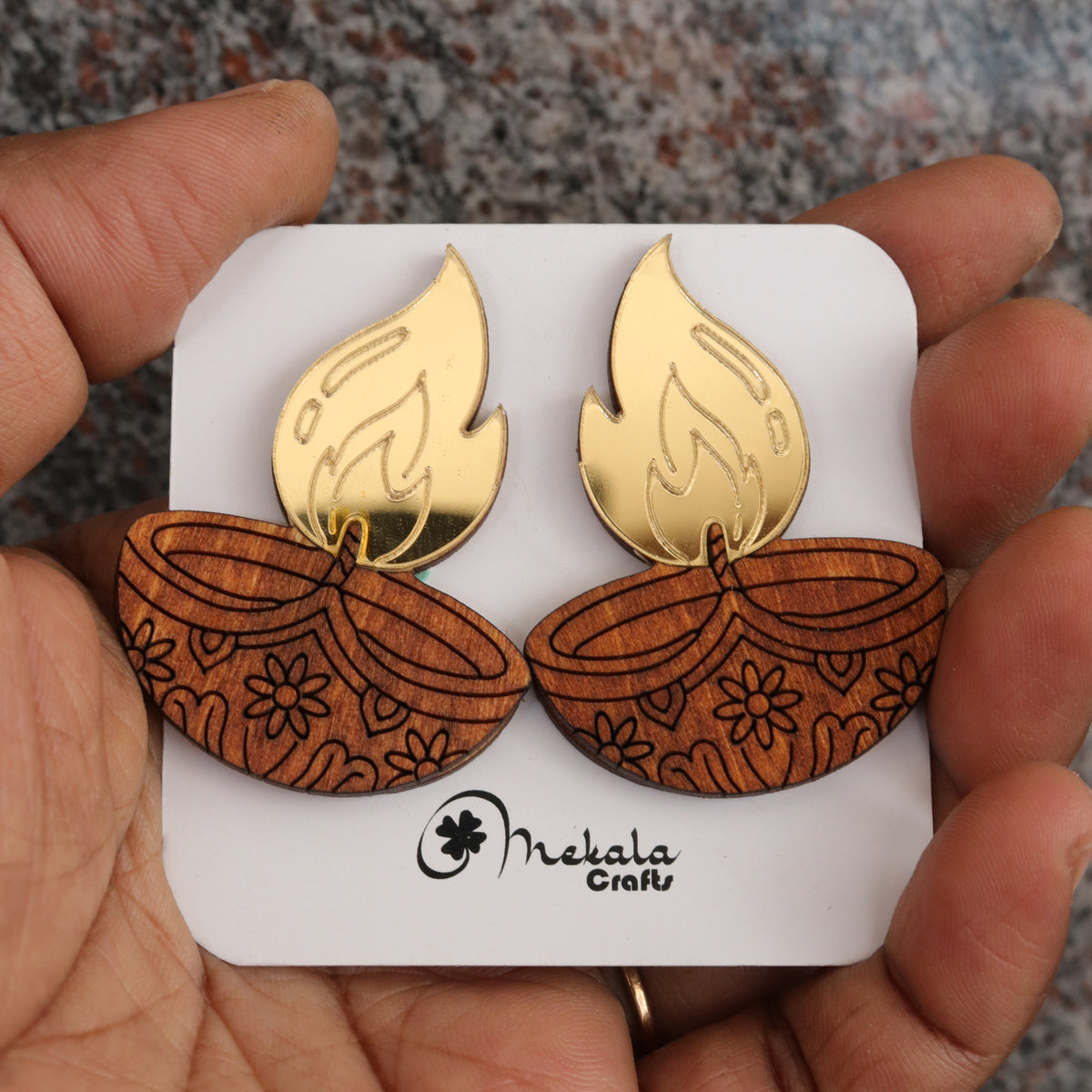 Close-up of wooden diya lamp earrings with gold acrylic flame and engraved floral pattern, handmade by Mekala Crafts